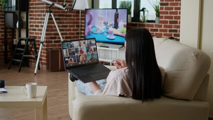 Poster - Woman working remotely from home while in online meeting videocall on laptop sitting on sofa in apartment. Freelancer working from home while discussing with coworkers on internet conference.