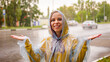 Young woman in raincoat on street in rain. Positive female catching raindrops with hands, enjoying weather.
