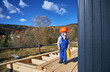 © anatoliy_gleb - Boy toddler playing as builder on construction site. Child carpenter in orange helmet and blue overalls learning to build wooden frame house outdoor on sunny day. Carpentry and workshop concept.