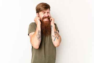 Young caucasian red-haired man isolated on white background covering ears with fingers, stressed and desperate by a loudly ambient.