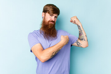 Young caucasian red-haired man isolated on blue background showing strength gesture with arms, symbol of feminine power