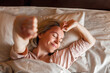 © Tatyana Gladskih - Happy middle aged woman sits on bed and stretching arms