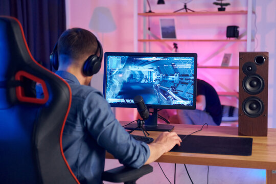 Sitting on the chair. Online streamer playing FPS shooter game at home