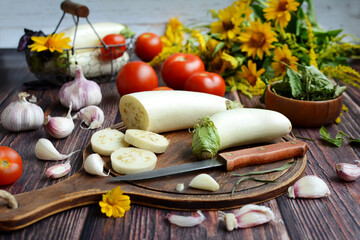 Wall Mural - White eggplants on a wooden board, tomatoes, garlic, herbs, yellow flowers on a rustic table. Cooking vegetables, diet