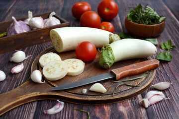 Wall Mural - Close-up cutting board with white eggplant, tomatoes and garlic.Healthy food. Kitchen, autumn, harvest.