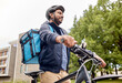 © Syda Productions - food shipping, profession and people concept - happy smiling indian delivery man with thermal insulated bag and bicycle on city street