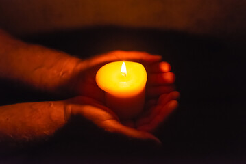 Wall Mural - Burning candle in a mans hand religion concept.Candle in hands on a dark background.