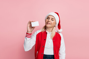 Wall Mural - blonde woman in red santa hat holding empty driving license isolated on pink