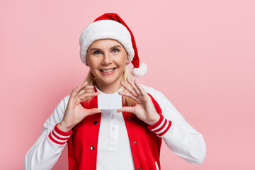 Wall Mural - cheerful woman in santa hat holding empty driving license isolated on pink