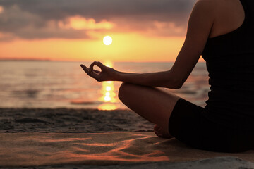 Wall Mural - yoga, mindfulness and meditation concept - close up of woman meditating in lotus pose on beach over sunset