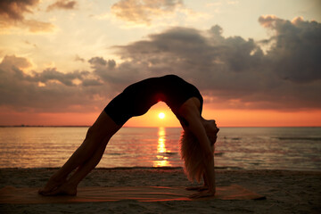 Wall Mural - fitness, sport, and healthy lifestyle concept - woman doing yoga bridge pose on beach over sunset