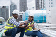 © amorn - Group of African American engineer worker working in sewer pipes area at construction site. Male engineer and woman engineer work with laptop computer for maintenance sewer pipes, water tank