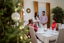A Group Of Friends Spend Christmas Together At Home, A Christmas Tree With Baubles And Lights, An Elegantly Set Table, Waiting For Other Guests To Arrive, Chatting