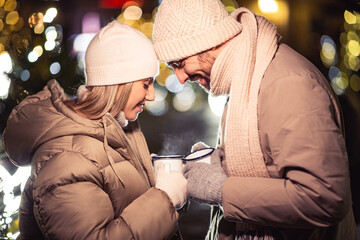 Poster - people, holidays and leisure concept - happy couple with tea cups over christmas lights