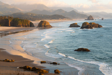 late evening sunlight falls across cannon beach and the sea stacks on the oregon caost alongside the