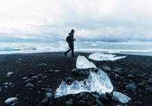 Person On Black Beach Surrounded By Pieces Of Ice