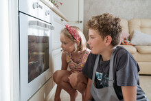 Children Look Into The Oven And Wait For The Food To Be Cooked.