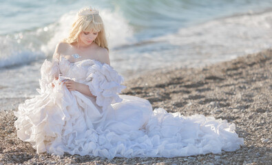 Young brunette woman in summer white dress standing on beach and looking to the sea.