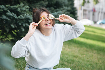 Wall Mural - A young woman eating sushi in the park, picnic in nature.