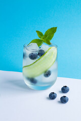 Wall Mural - Summer drink with cucumber, mint and blueberry in the drinking glass on the colored  background. Location vertical.