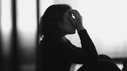 Monochromatic shot of desperate young woman suffering from emotional pain sitting on floor at home