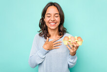 Young Hispanic Woman Holding Eggs Isolated On Blue Background Laughs Out Loudly Keeping Hand On Chest.