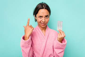 Wall Mural - Young hispanic woman holding pills isolated on blue background showing a disappointment gesture with forefinger.