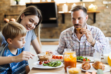 Wall Mural - Young mother feeding her small boy while having breakfast in the kitchen