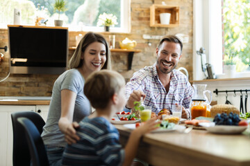 Wall Mural - Happy father feeding his  small boy while having breakfast in the kitchen