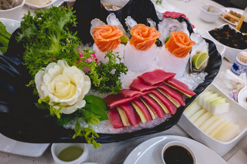 Beautiful and delicious shell arrangement of sashimi slices of sushi on ice with tuna and cucumber, salmon in form of flowers and green decoration in a table with food