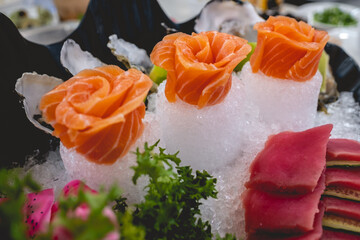 Beautiful and delicious shell arrangement of sashimi slices of sushi on ice with tuna and cucumber, salmon in form of flowers and green decoration in a table with food