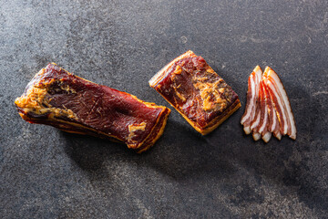 Canvas Print - Whole and sliced smoked bacon on black table.