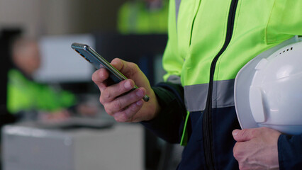 Cropped shot of builder chat on smartphone holding hardhat