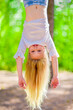 Leinwandbild Motiv Cheerful young girl with long blond hair hangs upside down outdoors in the park. Sunny summer day