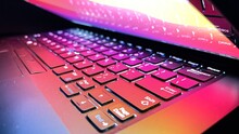 Studio Shot Of Closeup Of Laptop Keyboard Illumination, Backlit Keyboard Lit With Colorful Desktop Screen Wallpaper In A Dark Room	
