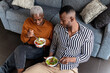 © Ezequiel Giménez/Stocksy - Hungry black couple eating yummy salad sitting on floor