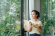 © Marc Tran/Stocksy - Young woman having healthy lunch at workplace, standing at window