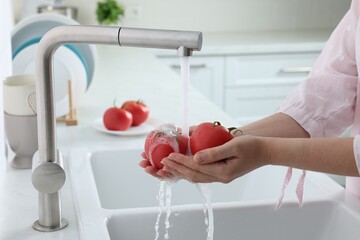 Wall Mural - Woman washing fresh ripe tomatoes under tap water in kitchen, closeup