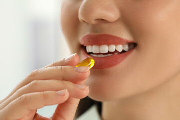 Poster - Young woman taking dietary supplement pill on blurred background, closeup