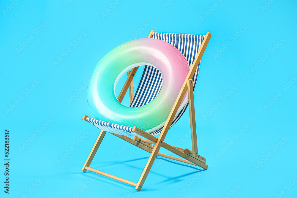 Wooden deck chair with inflatable ring on blue background