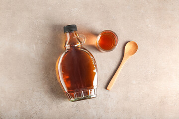 bottle and glass of maple syrup on light background