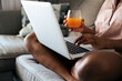 © David Prado/Stocksy - Crop black man using laptop on sofa