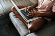 © David Prado/Stocksy - Crop woman using laptop on sofa