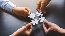 Close Up Four Hands Holding Pieces Of White Jigsaw Puzzle, Joint Path To Problem Solution, Find Way Out Exit Of Difficult Situation. Support, Teamwork Concept.