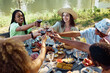 © Seventyfour - High angle diverse group of young people toasting with wine glasses during dinner party outdoors in Summer