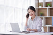 © David - Charming Young business Asian woman manager with a smile working on a laptop holding document and talking on a mobile phone at the office.