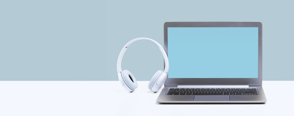 Wall Mural - Laptop. Mockup blue screen and headphones on white desk and plain background banner. Distant learning. working from home, online courses or support minimal concept. Helpdesk or call center headset