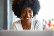 © fotofabrika - Smiling young african woman sitting with laptop in cafe