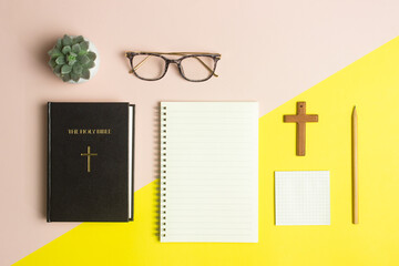 Wall Mural - Bible with notebook, cross and glasses over the pink and yellow background.