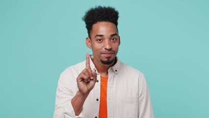 Wall Mural - Young secret man of African American ethnicity wear shirt t-shirt look aside say hush be quiet with finger on lips shhh gesture say know wave finger isolated on plain pastel light blue cyan background